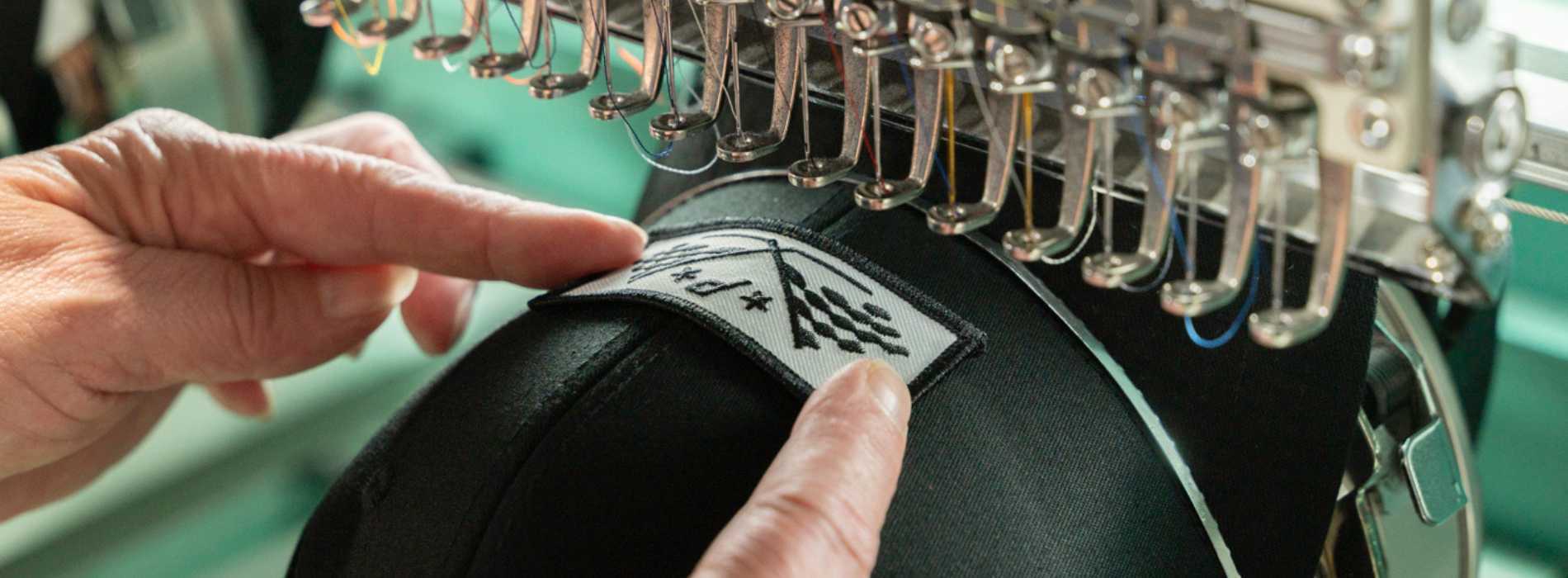 a black hat getting a logo embroidered on it by an embroidery machine
